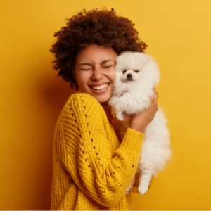 woman in yellow sweater happily cuddling pomeranian in front of yellow background