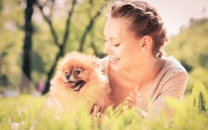 happy girl cuddling Pomeranian in grass