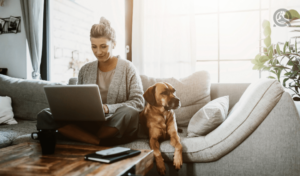 woman sitting on couch, looking at laptop, with dog next to her
