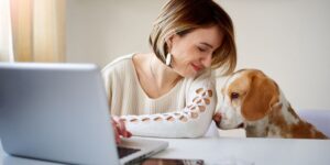 Caucasian businesswoman playing with dog in home office. Dog daycare article.
